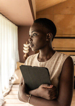 Woman Stands by Window Holding a Tablet in a Well-Lit Room