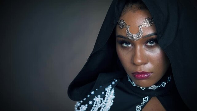 Closeup fantasy african american woman voodoo witch conjuring. Art video beauty lips headshot. Girl vampire looking at camera hypnotizes eyes sexy face. Gothic style Black dress hood.
