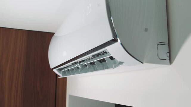 Close-up shot indoor unit air conditioning in room attached on wall. Flow of cold, frosty air, cooling house. Modern technologies. Turns on wing goes down, blinds are opened, drives cold air. Video 4k