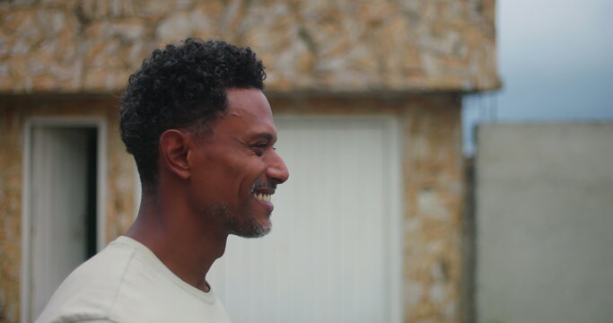 Man of African descent walking in profile, smiling, looking ahead, relaxed demeanor, joyful presence, urban street background, casual attitude, natural expression, confidence