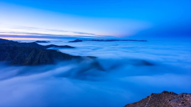 Mountains Covered by a Majestic Cloud Inversion Flowing Through an Alpine Valley at Sunset, with a Vibrant Blue Sky Above.