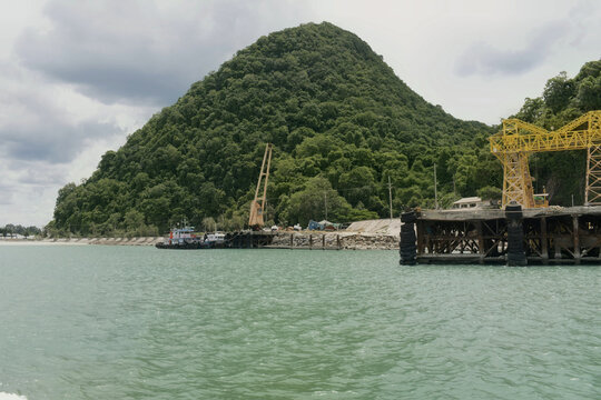 an offshore view approaching a small industrial loading terminal and pier structures nestled along the lush green hilly coastline of khanom, thailand 