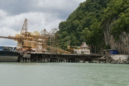 industrial cargo loading facilities stand beside dramatic limestone cliffs along the khanom coastline in southern thailand, contrasting heavy industry with a tropical coastal landscape