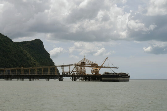 industrial belt conveyor system terminal loading mineral materials into large cargo barge vessel at khanom coastline jetty facility