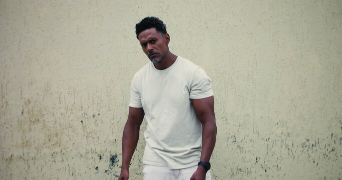 Man of African descent standing against textured wall, pointing forward with serious expression, confident and assertive body language, confrontational stance, strong presence