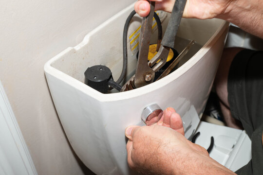 Hand using wrench to remove toilet handle.  Household repairs.