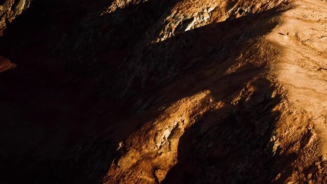Sunlight creates shadows on rocky terrain. The landscape is dry and rugged, with varying colors of brown and orange. This scene captures the natural beauty of mountains.