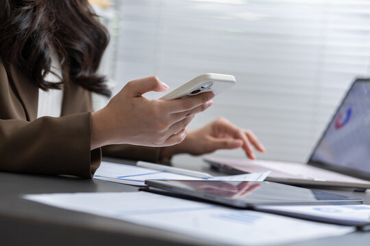 Hand smartphone laptop tablet document office worker using mobile phone beside computer digital tablet and paperwork on desk during business task