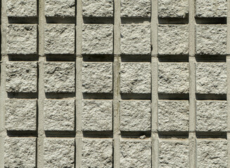 Horizontal close up photo of a modern concrete block wall. Detailed architectural background with a geometric pattern of rough grey square stone modules and deep shadow lines © Marco