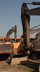Słoneczne ujęcie ciężkich maszyn budowlanych z żółtą koparką gąsienicową na pierwszym planie, zaparkowanych na placu budowy. © tomo81