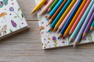 Obraz premium Colorful pencils rest on a floral notebook. Wooden surface adds a warm, rustic tone. Bright hues suggest creativity and joy. Ideal for art, education, or nature-themed projects
