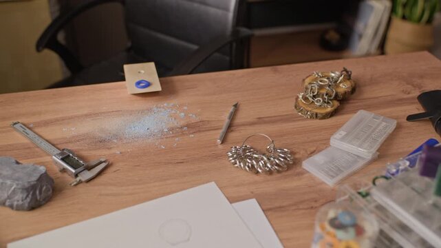 No people close up shot of jeweler workbench displaying ring sizer, caliper, carving knife, and blue wax shavings during slow camera pan. For handmade jewelry brand promotions, craft marketing