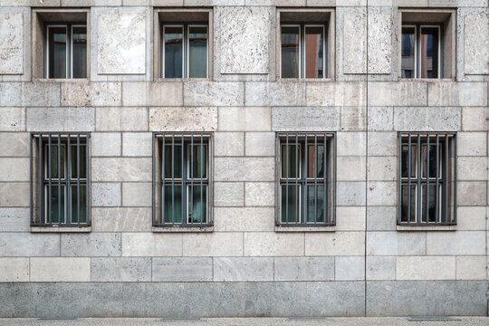 A straight-on, eye-level shot of a historic stone building facade in Berlin, showing a repetitive pattern of windows on two levels, with the bottom row featuring security bars.