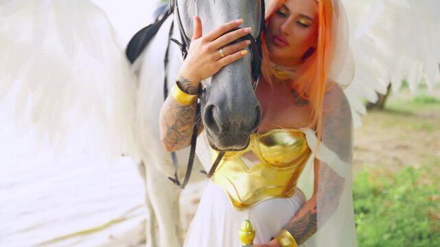 Art portrait Fantasy woman with horse. Fashion model posing queen hand stroking touching embracing pegasus muzzle white horse bird wings. Elf girl sexy eyes beauty face love. sun light green tree sea.