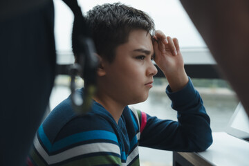 Cinematic portrait of thoughtful boy sitting indoors and looking into the distance. Quiet childhood moment, reflection, introspection, emotions, imagination and personal growth concept. © Anchalee