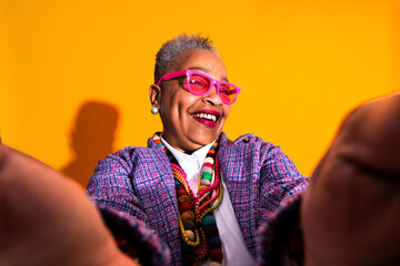 Senior woman smiling taking a colorful selfie - Old hispanic grandmother wearing fashionable modern...