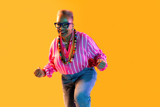 Senior woman smiling and dancing for happiness and energy - Old hispanic grandmother wearing fashionable modern clothing on colorful background, concepts about elderly, aging, diversity 