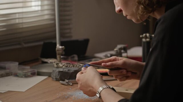 Close up of young adult Caucasian woman jeweler filing blue wax ring model at workbench. Clip perfect for marketing handmade jewelry brands, craft workshops, and creative entrepreneurship