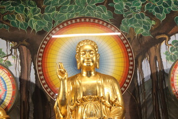 Obraz premium Golden buddha statue in meditation pose under painted bodhi tree wall background.