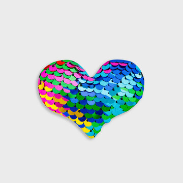 Colorful sequin heart isolated on white background, vibrant rainbow love symbol of shiny overlapping scales, bright decorative romantic element for celebration, creativity, and modern pop art style.