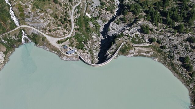 Barrage courbe retenant un lac turquoise en montagne, vue a&eacute;rienne