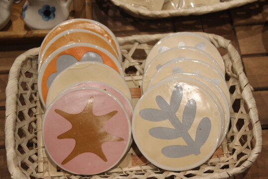 Round ceramic coasters with painted plant and organic leaf motifs in wicker basket.