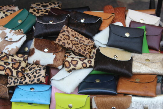 Pile of assorted handmade leather wallets and purses on display at outdoor market.