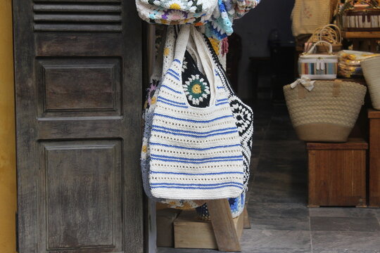 Handmade striped crochet shoulder bag hanging on wooden door frame inside boutique.
