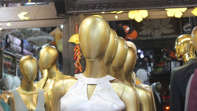 Group of golden mannequins in front of clothing shop showing stylish fashion items.