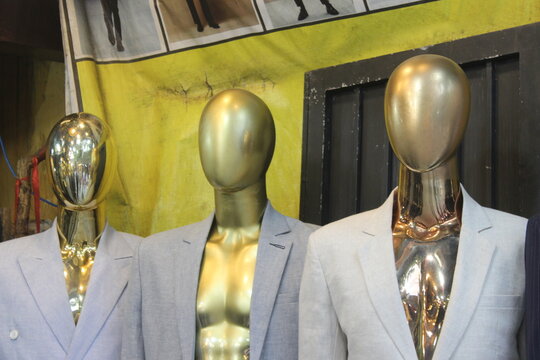 Three headless golden mannequins wearing formal blazers standing in clothing store.