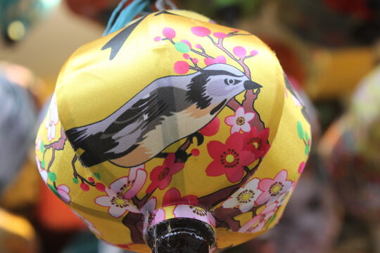 Decorative fabric lantern with bird illustration hanging in a traditional market.