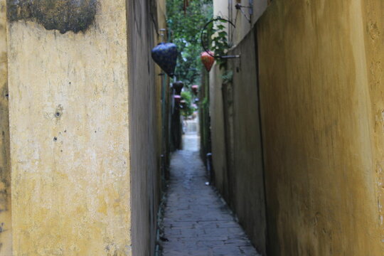 View through narrow urban alleyway with aged yellow walls and hanging light decor.