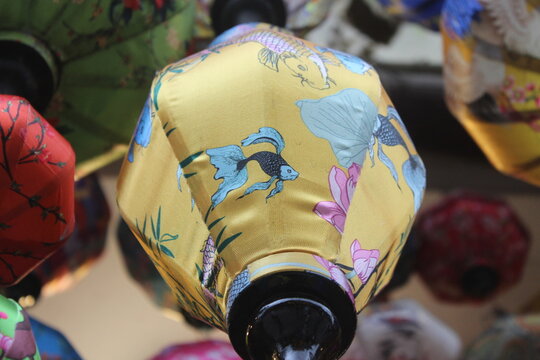 Golden yellow lantern with koi fish and floral painting in a traditional setting.