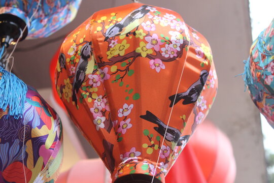 Orange silk lantern featuring intricate bird and floral blossom pattern in market.