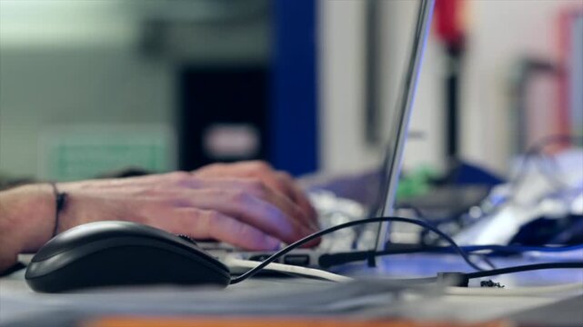 mani di giovane uomo adulto e tecnico informatico mentre  lavora ad un progetto e scrive al computer su un bancone pieno di oggetti