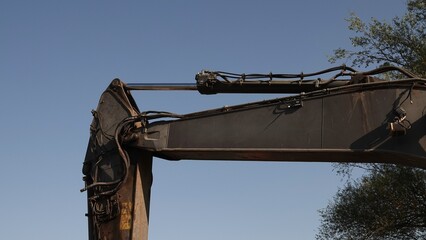 Poziome zbliżenie na siłownik hydrauliczny oraz metalową konstrukcję ramienia ciężkiej koparki gąsienicowej na tle bezchmurnego nieba. © tomo81