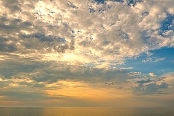 Fototapeta premium Scenic sunset sky filled with dramatic fluffy clouds over the calm sea horizon at golden hour.