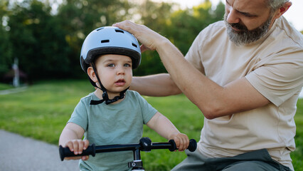 Obraz premium Father fastening helmet on toddler son before bike ride.