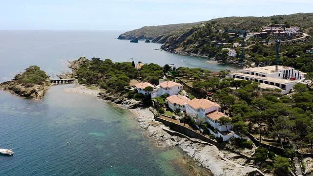 Aerial view of Platja Sa Conca, a secluded Costa Brava beach surrounded by pine-covered cliffs, elegant hillside villas and the crystal-clear waters of the Mediterranean Sea. 
