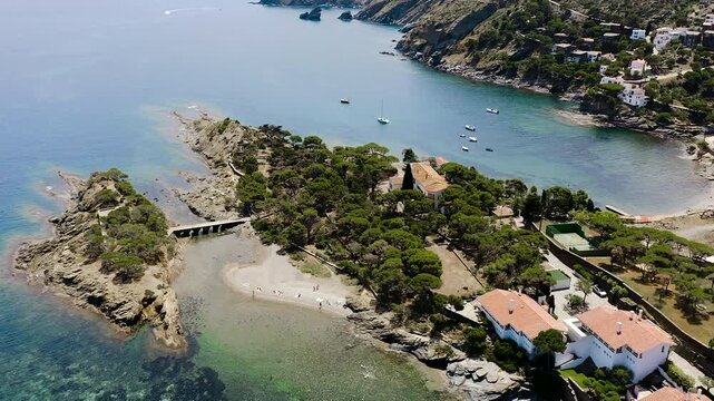 Aerial view of Platja Sa Conca, a secluded Costa Brava beach surrounded by pine-covered cliffs, elegant hillside villas and the crystal-clear waters of the Mediterranean Sea. 