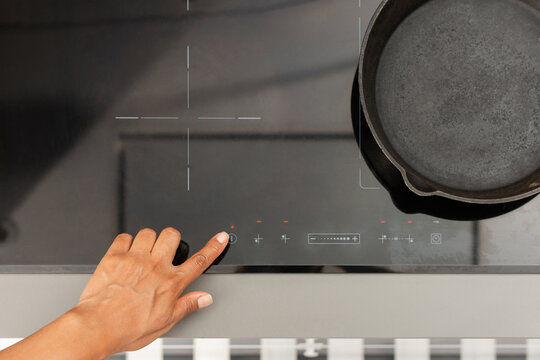 Birds eye view of turning on modern induction cooktop with cast iron skillet