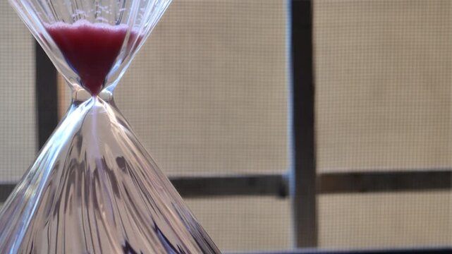 Hourglass with crimson red sand pouring in close-up static shot