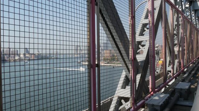 Williamsburg Bridge in Brooklyn, New York City, United States. Transport metallic bridge near Marcy Av subway station and Domino park in Williamsburg. East River and Manhattan view thru pink fence.