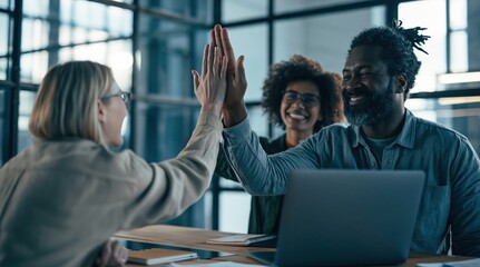 Obraz premium Happy diverse coworkers high-fiving at office with laptop