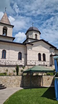 Outdoor view of Varzaresti Monastery with a cobblestone courtyard and a prominent bell tower with a dark dome topped with Christian crosses under a beautiful sky