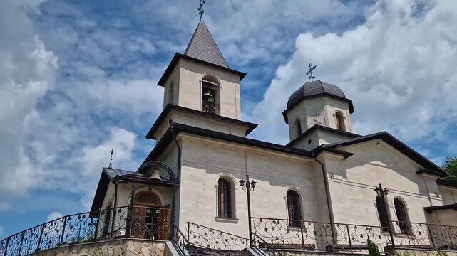 Outdoor view of Varzaresti Monastery with a cobblestone courtyard and a prominent bell tower with a dark dome topped with Christian crosses under a beautiful sky