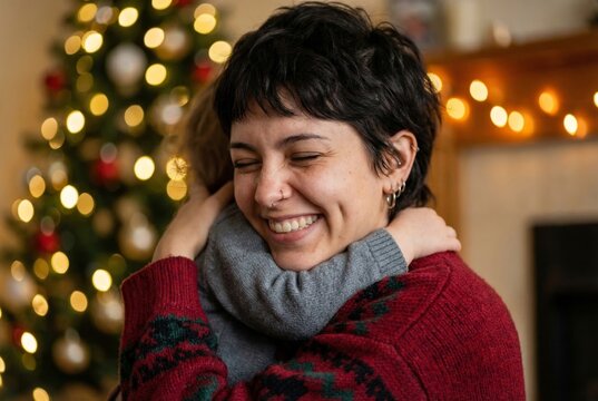 Joyful short haired mother laughing while tightly hugging her child next to Christmas tree