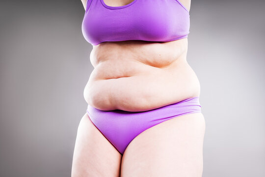 Overweight woman with belly fat in underwear on gray background. Obesity, weight loss, diet and body positivity concept