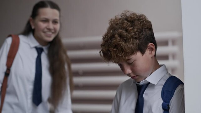 Caucasian teenager boy looking down with lowered head while Caucasian teenager girl mocking and laughing at him in background. Footage ideal for school bullying awareness campaigns