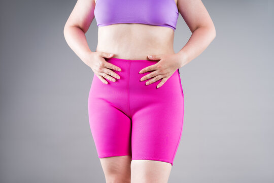 Overweight plus size woman struggling to pull up tight pink neoprene slimming shorts. Weight loss, shapewear and body shaping concept